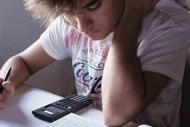 Student sat at desk looking at calculator 